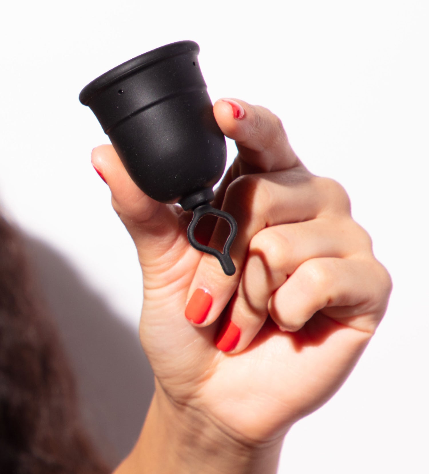 Hand holding a black menstrual cup against a white background