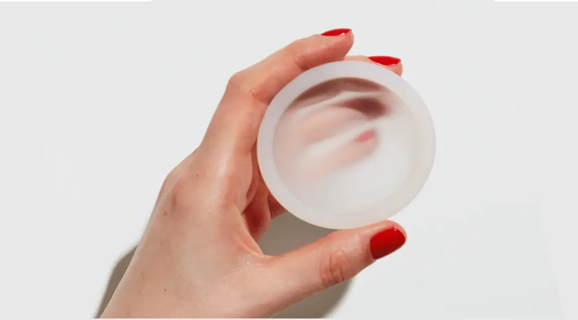 Hand holding a reusable menstrual disc against a white background