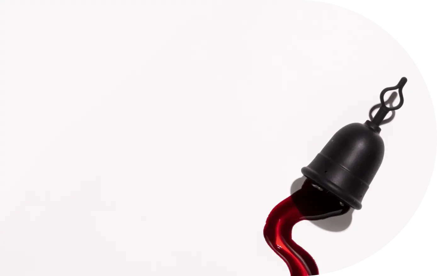 Menstrual cup with loop stem shown draining blood on a white background