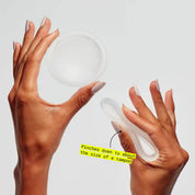 Hands holding and pinching a reusable menstrual disc, showing its size when compressed
