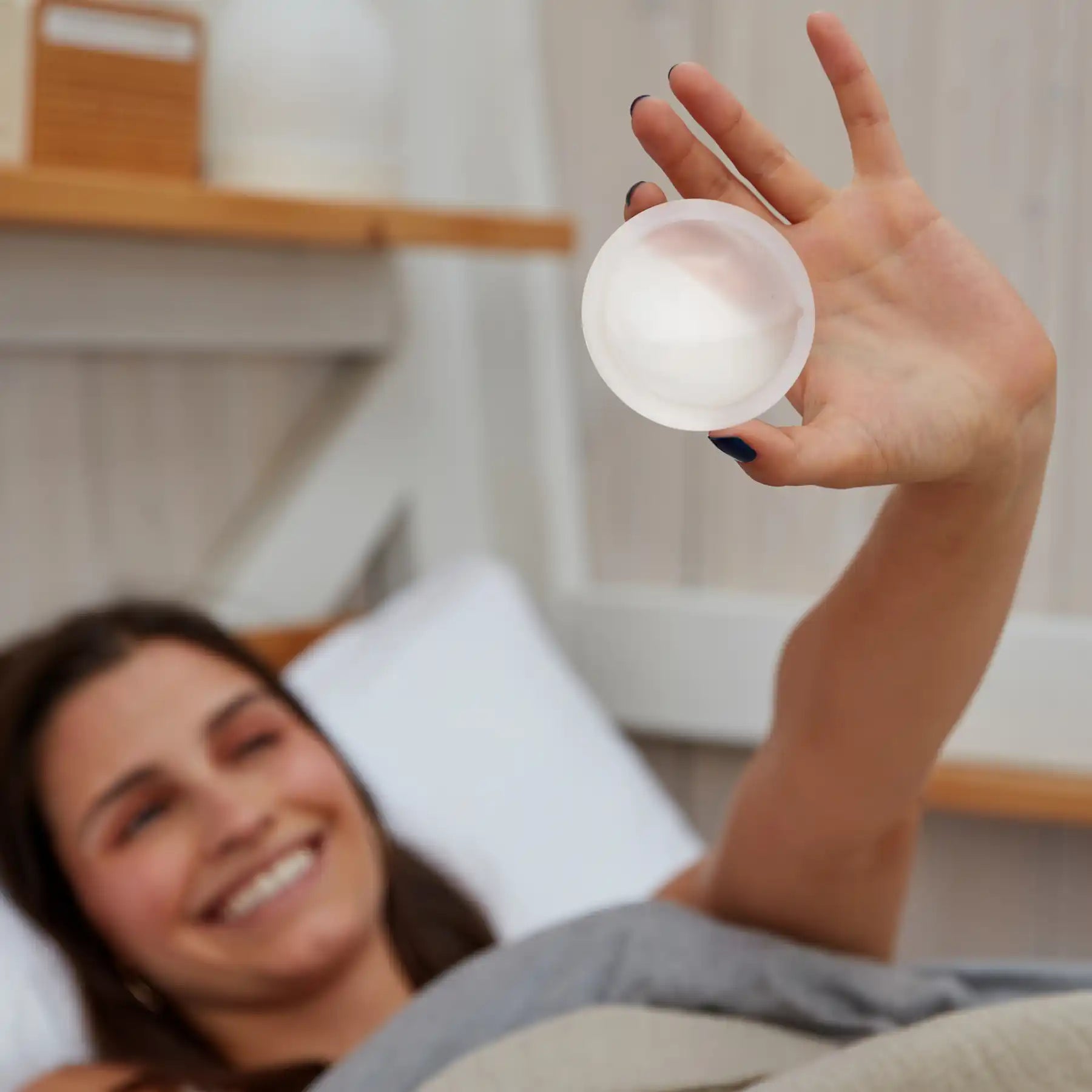 A person happy and smiling holding a Flex Reusable Menstrual Disc up in front of her face
