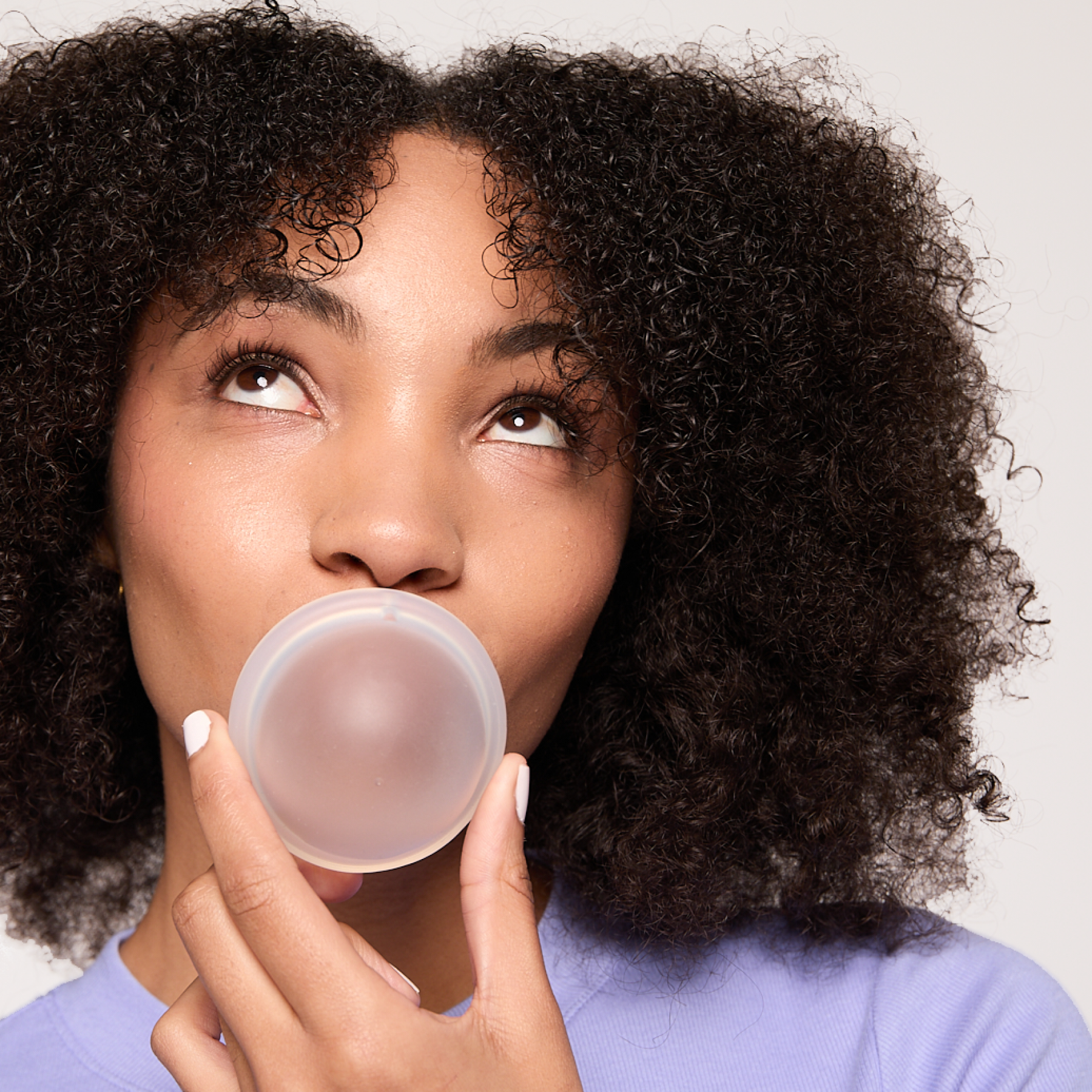 Person holding a reusable menstrual disc in front of their mouth