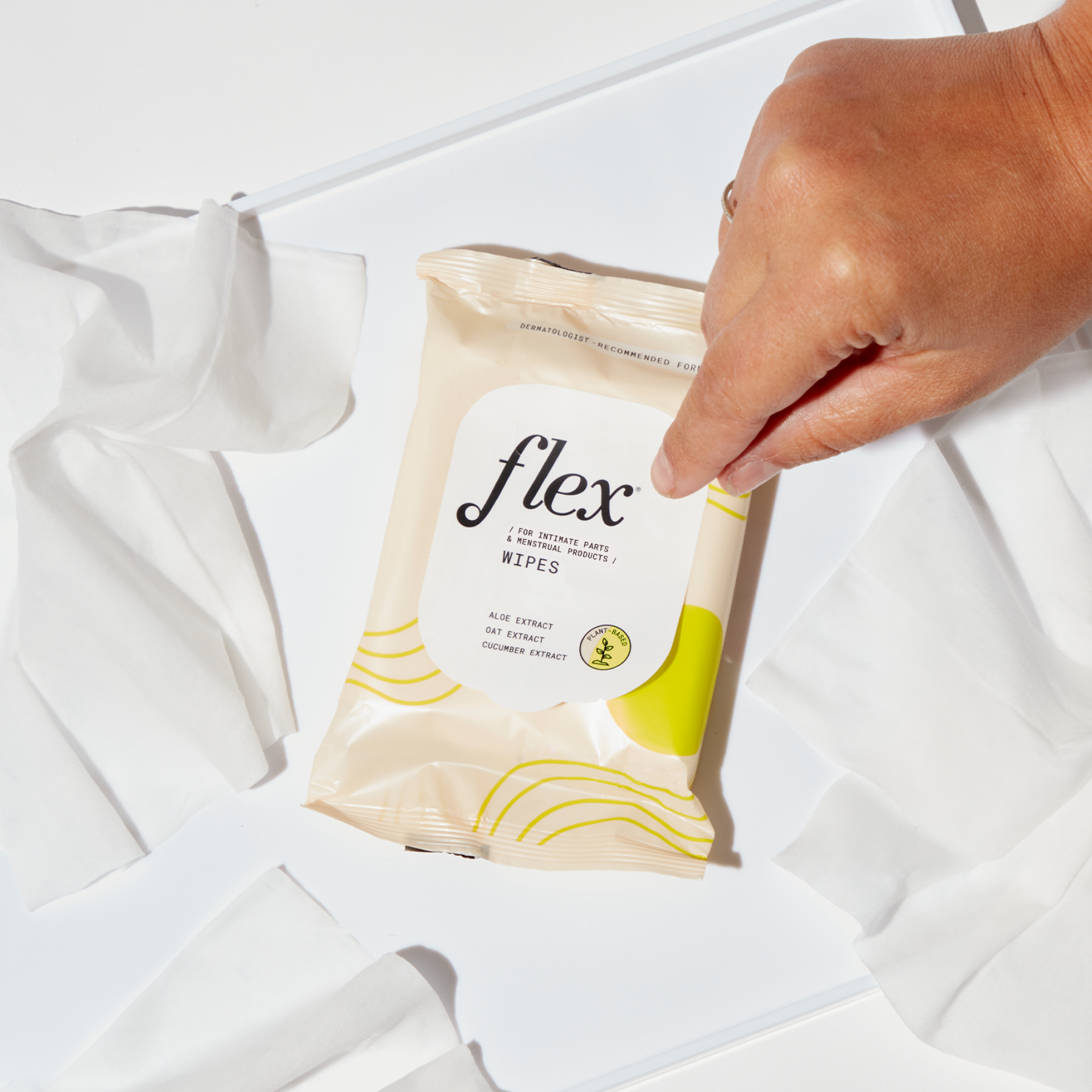 Hand picking up pack of Flex wipes next to unfolded wipes on a white surface