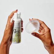 Hands holding a foaming cleanser bottle and a menstrual disc