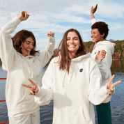 Three people wearing branded hoodies smiling and posing outdoors near a lake