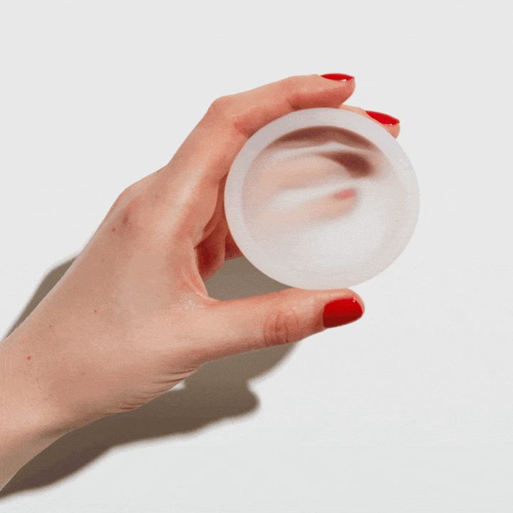 Hand holding flexible reusable menstrual disc to show pliability and shape