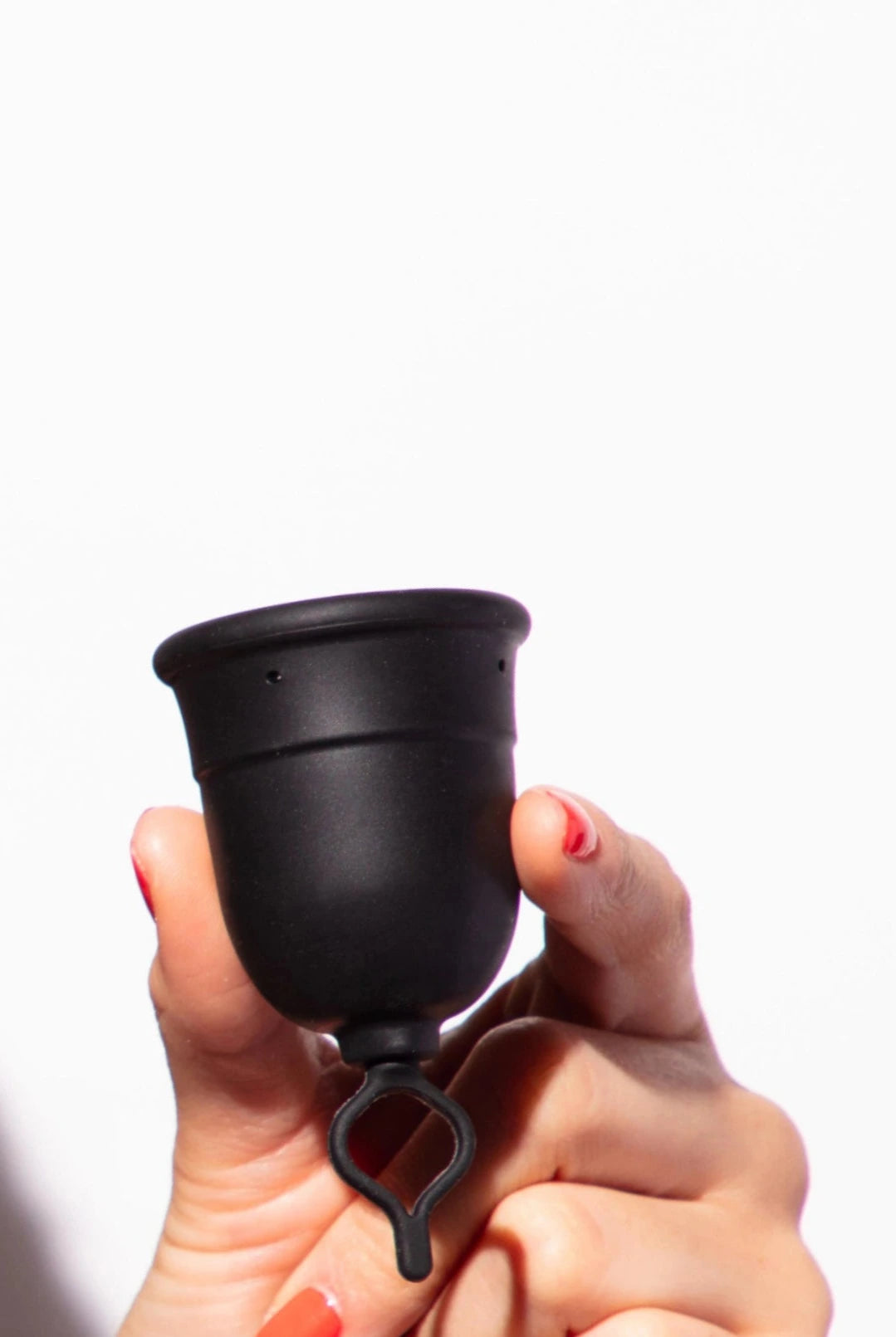 Hand holding a menstrual cup with a looped stem against a white background