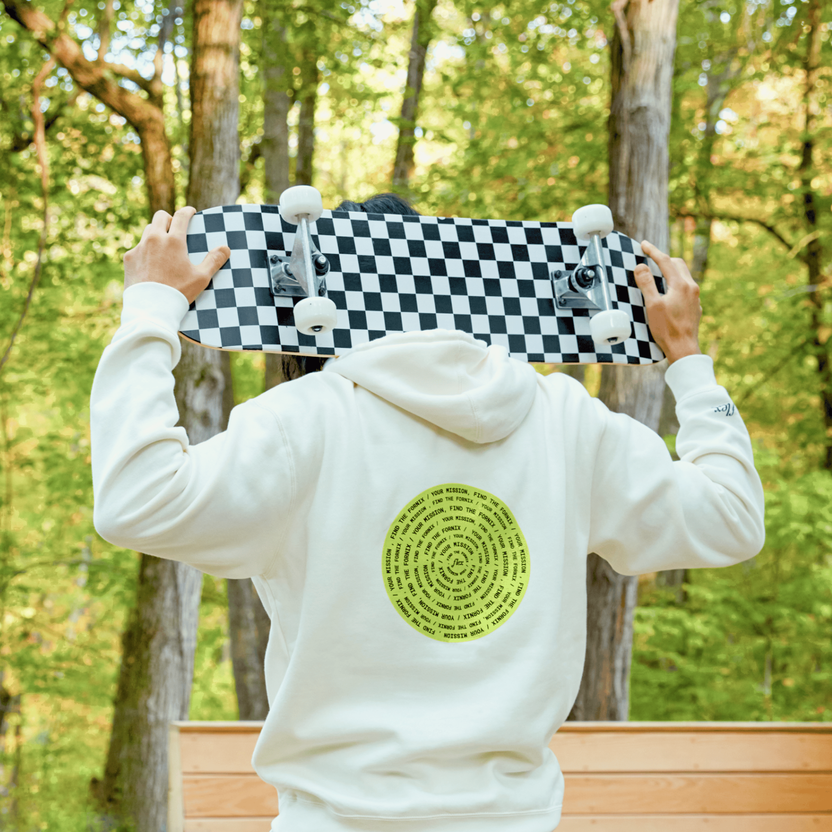 Person holding checkered skateboard behind head while wearing hoodie with circular text design