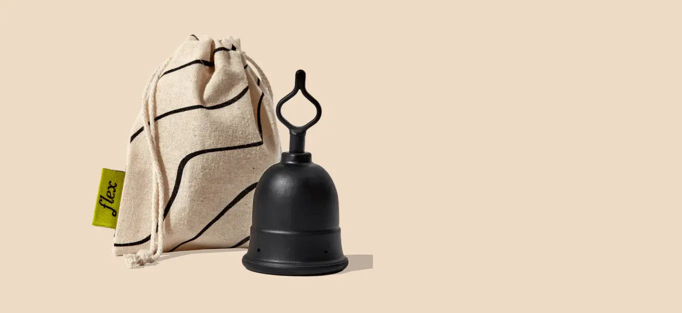 Silicone menstrual cup with loop-style stem next to a drawstring cloth pouch